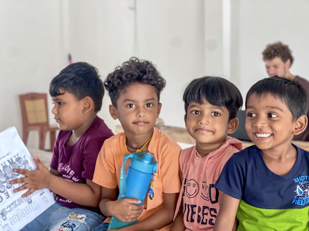 4 young kids smiling with a volunteer working in the background